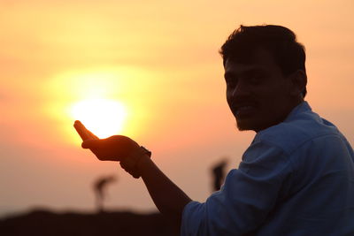 Portrait of man holding orange against sky during sunset