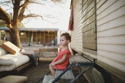 Side view of cute girl looking away while sitting on metallic steps at farm