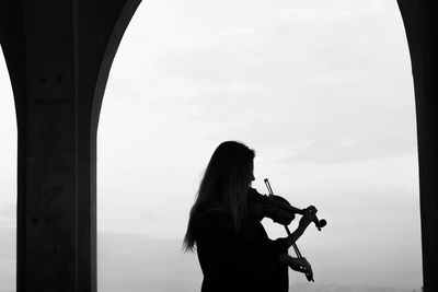 Silhouette woman playing violin against sky
