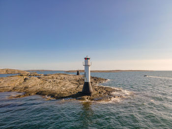 Lighthouse by sea against clear sky