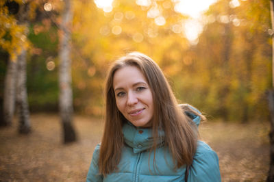 Portrait of smiling young woman standing against trees during autumn