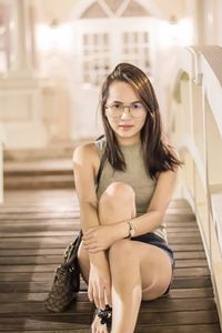 Portrait of beautiful woman sitting on footbridge against illuminated building at night