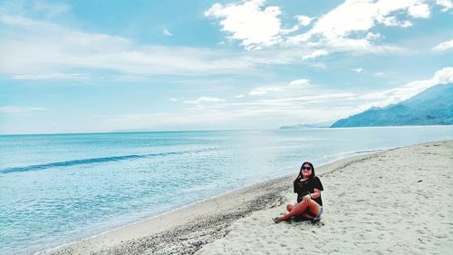 Man sitting on shore at beach against sky
