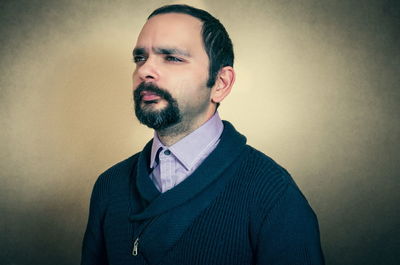 Thoughtful mid adult man looking away while standing against wall