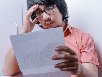 Portrait of young man holding eyeglasses against wall