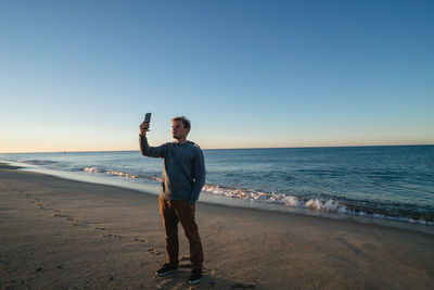 Full length of man photographing sea against clear sky