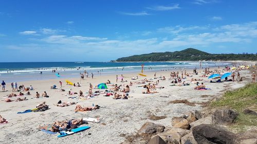 People relaxing on beach against blue sky