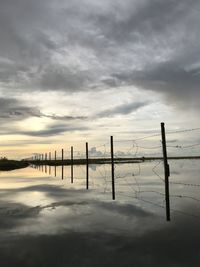 Wooden posts in sea against sky during sunset