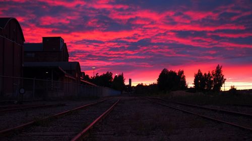 Railroad tracks by silhouette trees against orange sky