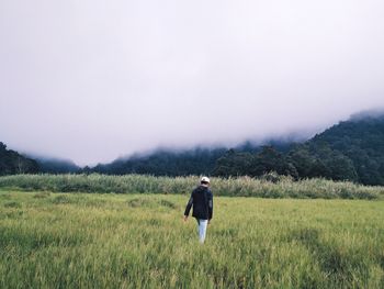 Rear view of woman walking on field against clear sky