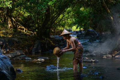 Side view of woman with basket standing in river at forest