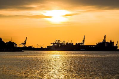 Silhouette cranes at commercial dock against sky during sunset