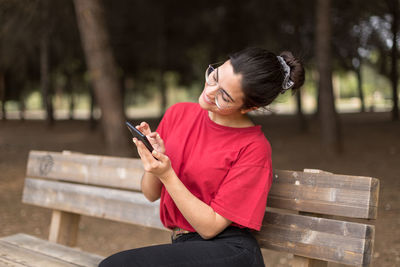 Young woman using phone while sitting on bench