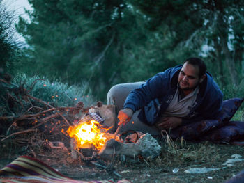 Young man sitting by bonfire in forest