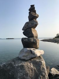 Stack of pebbles on rock by sea against sky