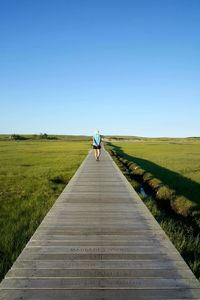 Rear view of woman walking on field against clear blue sky