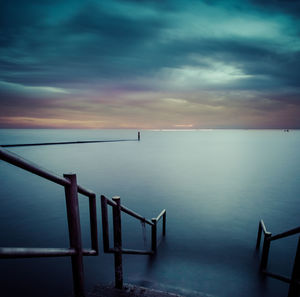 High angle view of steps leading towards sea against cloudy sky at dusk