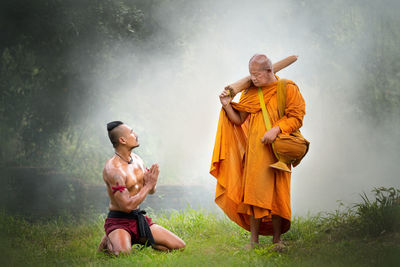 Shirtless man praying in front of monk