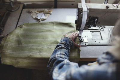 Cropped image of craftsperson sewing green fabric on machine at workshop