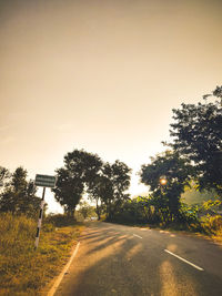 Empty road amidst trees against clear sky during sunset