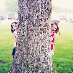 Playful siblings hiding behind tree at park
