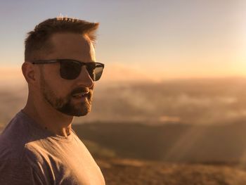 Portrait of young man wearing sunglasses against sky during sunset