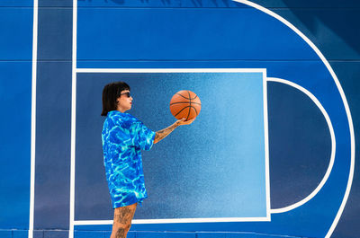 Caucasian girl with sunglasses and tattoos on a blue background with a basketball