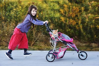 Full length of girl pushing cat in baby stroller on footpath