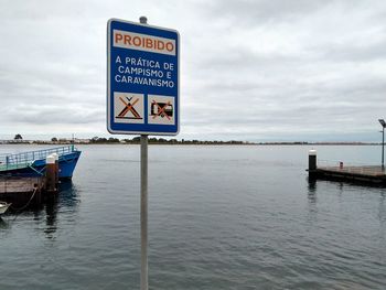 Information sign by sea against sky
