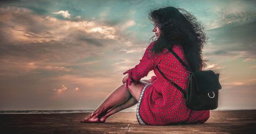 Woman sitting in sea against sky during sunset