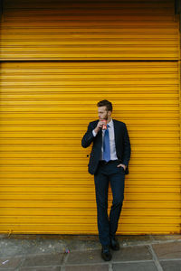 Full length of a young man standing against yellow wall