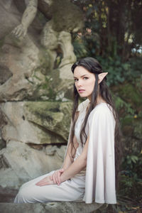 Portrait of fairy elf young woman sitting by fountain