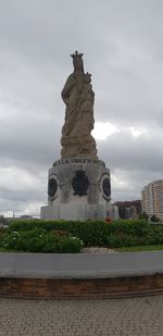 Statue in city against cloudy sky