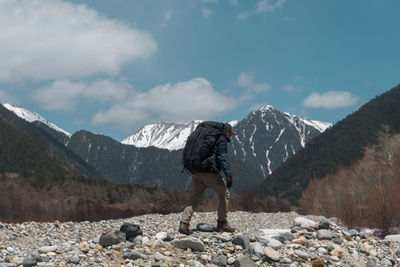 Side view of backpacker walking on land with mountains in background