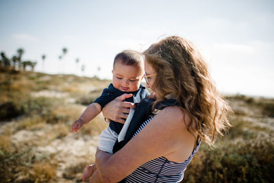 Grandmother holding & snuggling grandson while standing on beach