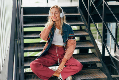 Young attractive blonde woman listening to music on headphones while enjoying outside.