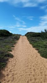 Dirt road amidst field against sky