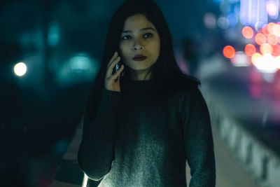 Portrait of young woman standing against illuminated lights