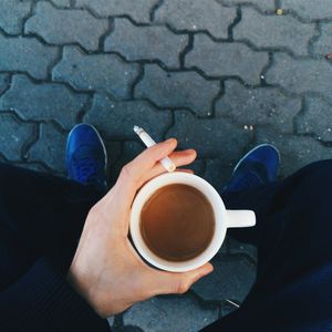 Low section of man holding cigarette and coffee cup