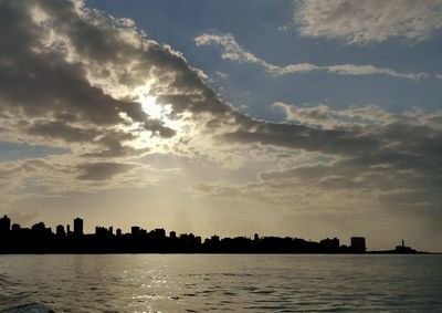 Silhouette buildings by sea against sky during sunset