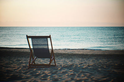 Empty chair on beach against sky