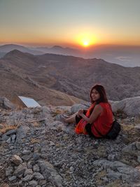 Young woman sitting on rock during sunset