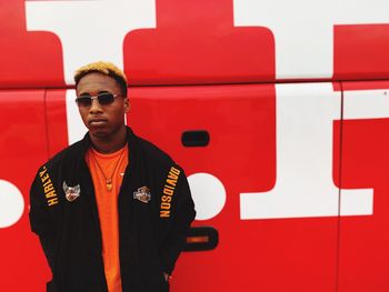 Portrait of young man standing against red wall