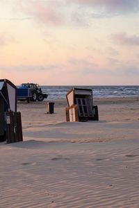 Hooded chairs on beach against sky during sunset