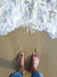 Low section of man standing at beach on sunny day