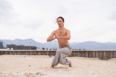 Shirtless man performing qi gong against sky