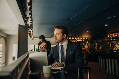 Thoughtful businessman with laptop sitting in hotel lounge while looking away