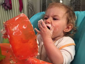 Close-up of messy baby boy eating while sitting on high chair at home