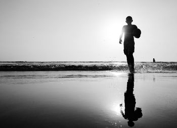 Silhouette man standing on beach against clear sky