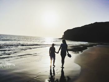 Silhouette women standing on beach against clear sky